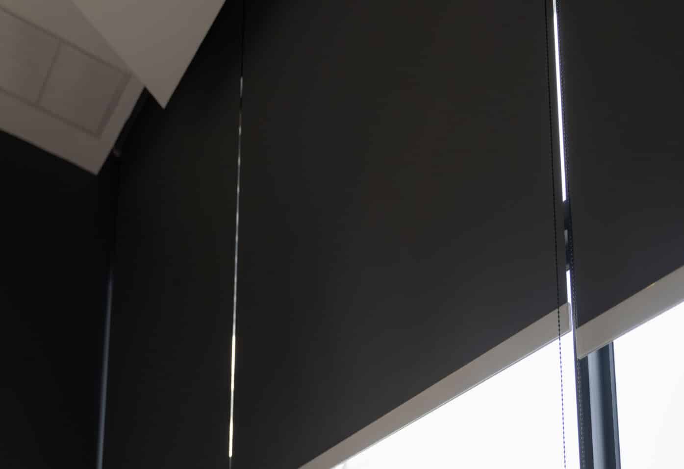 A large office window covered with black blackout blinds, blocking out light for privacy and darkness.