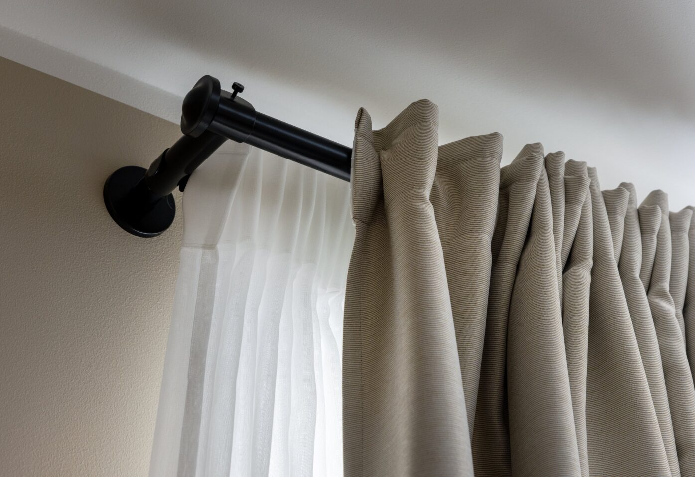 A curtain rod displays a hanging curtain, featuring visible hangers and the top section of the drapery.