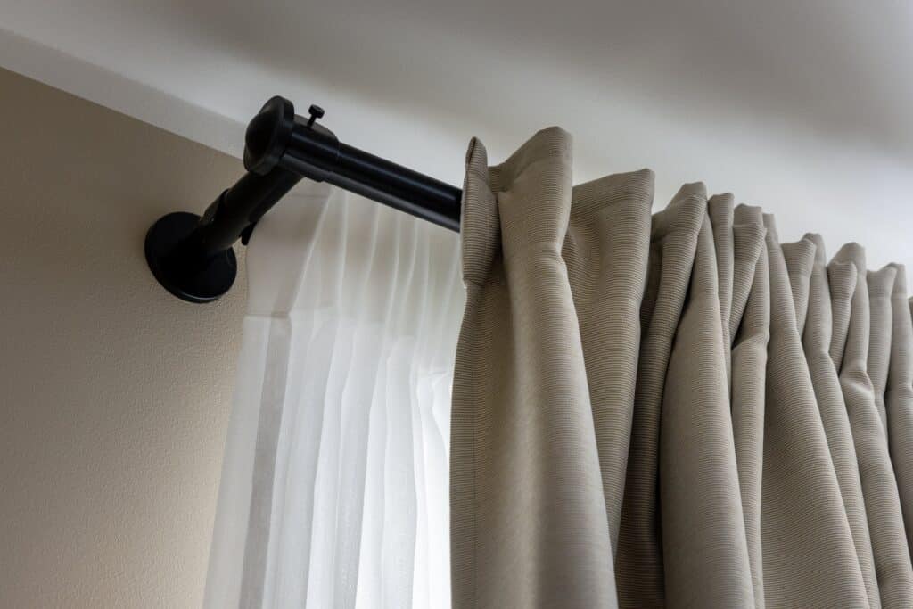 A curtain rod displays a hanging curtain, featuring visible hangers and the top section of the drapery.