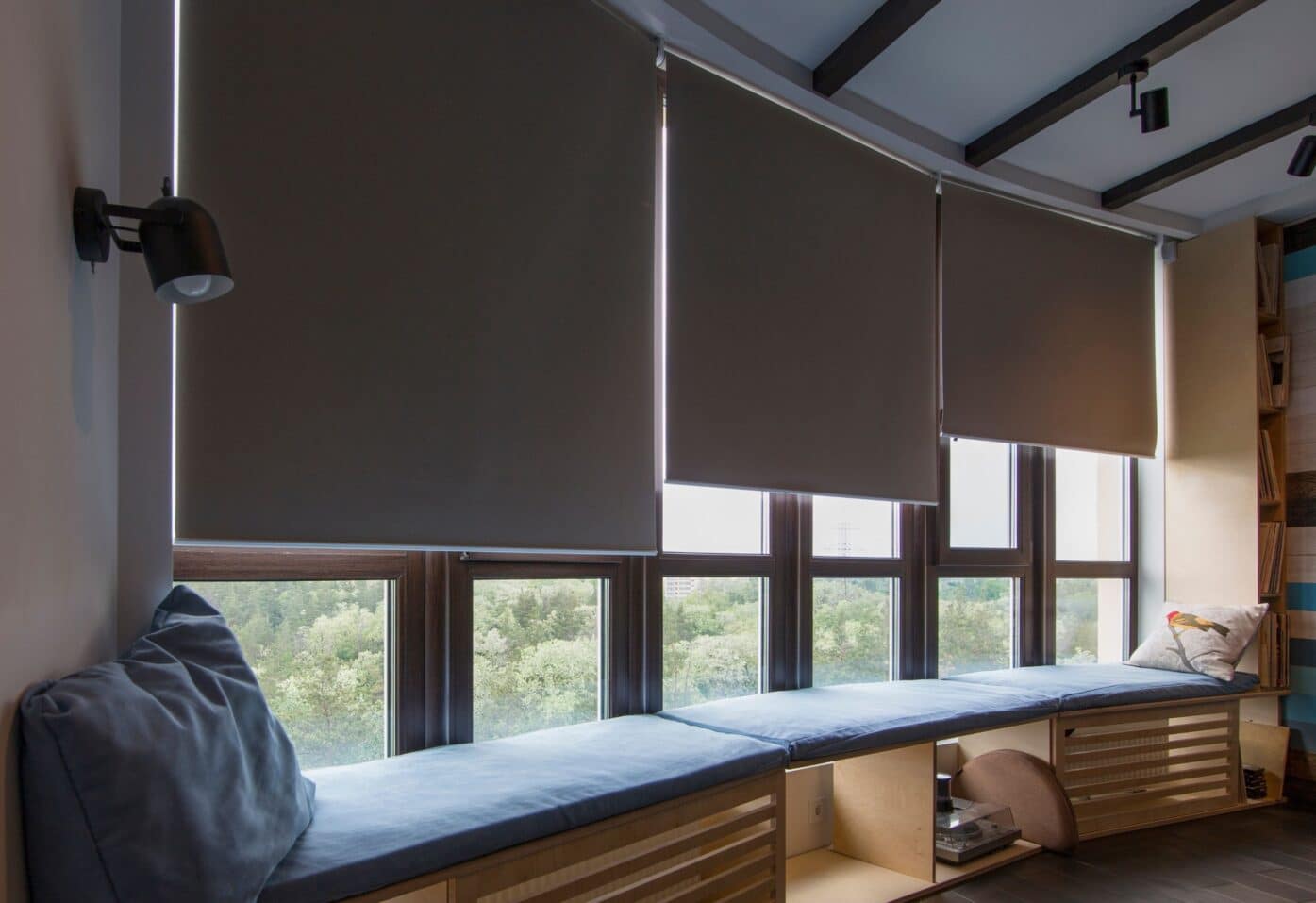A cosy window seat with a blue cushion, featuring roller blinds and a view through the window.